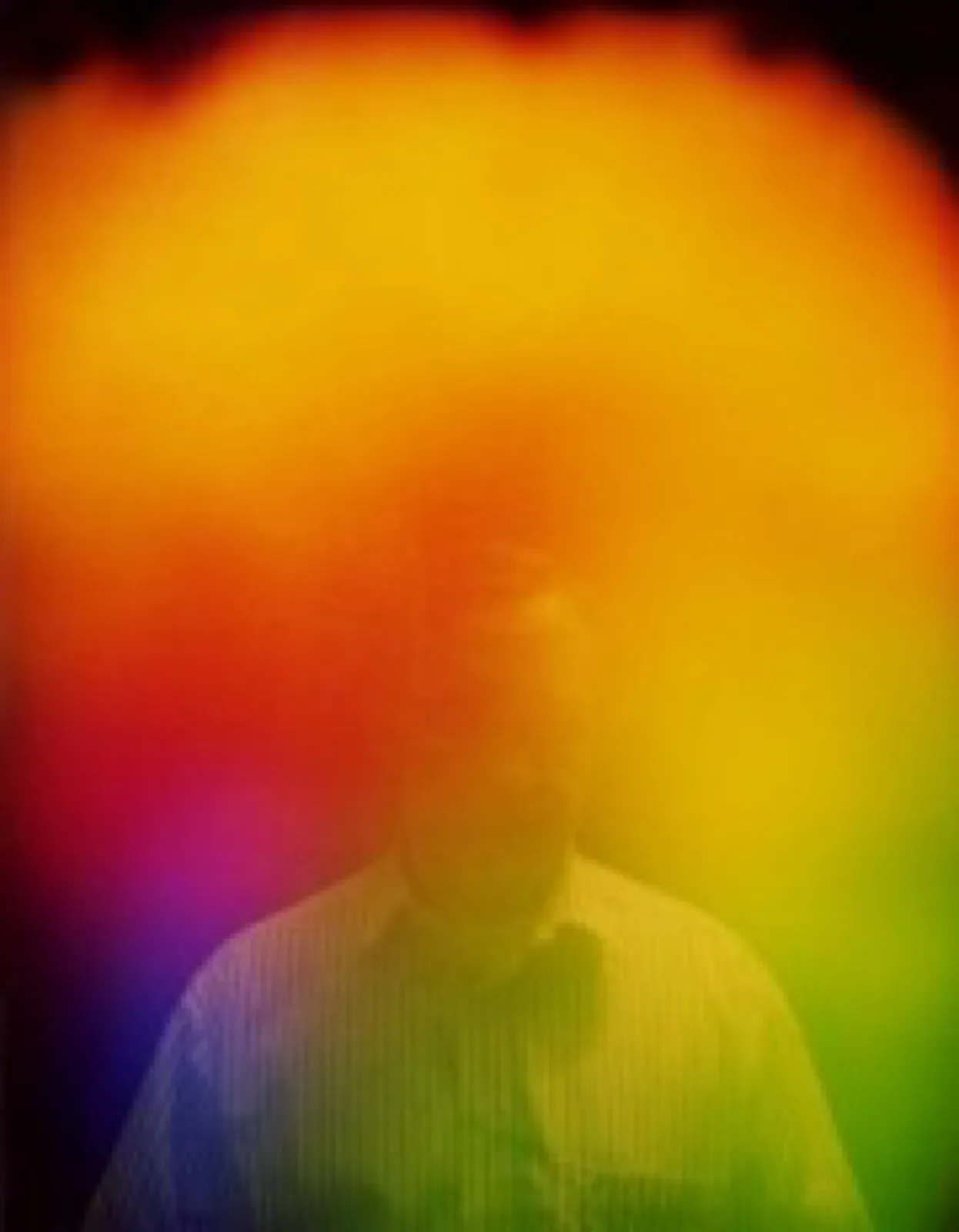 Aurafoto eines Mannes im gestreiften Hemd vor dunklem Hintergrund: Ein kräftiger orange-gelber Lichtschleier liegt über Kopf und Oberkörper, links unten violett und rot, rechts unten grün.