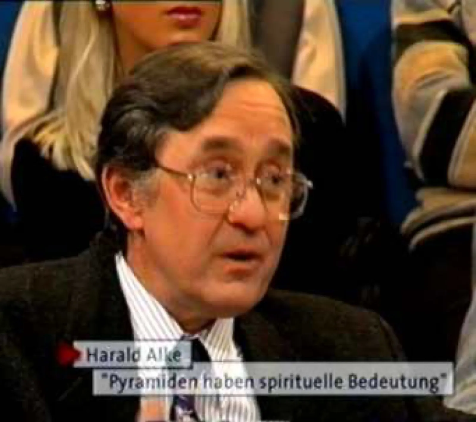 Standbild aus der ARD-Sendung „Fliege“ (1999): D. Harald Alke mit Brille, dunklem Sakko und gestreiftem Hemd spricht im Studio; eingeblendet sind sein Name und das Zitat „Pyramiden haben spirituelle Bedeutung“, dahinter sitzt Studiopublikum.