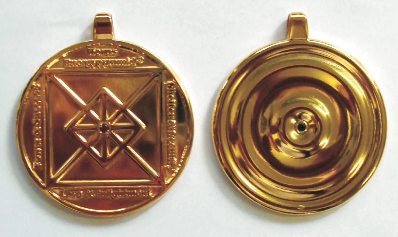 Vorder- und Rückseite eines goldglänzenden runden Anhängers mit Öse: vorn ein geprägtes Quadrat mit Diagonalen, Rautenornament und kleinem roten Stein sowie umlaufender Inschrift, hinten konzentrische Ringe mit einem blauen Stein in der Mitte.