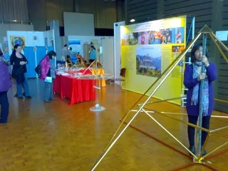 Messestand in einer Halle mit einer großen Horus Energiepyramide im Vordergrund, im Hintergrund Ausstellungstische mit roter Tischdecke und Informationsplakate.