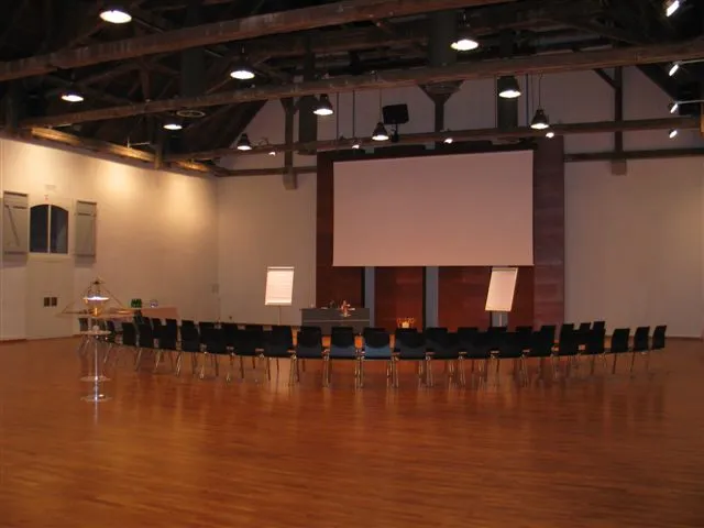 Leerer Seminarraum in der Karthause Ittigen mit Stuhlreihen im Halbkreis, Rednerpult, Projektionsleinwand und zwei Flipcharts – aufgebaut vor Seminarbeginn.