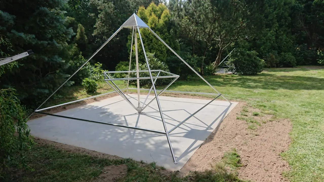Nahaufnahme einer Horus Energiepyramide Modell D auf einem quadratischen Betonsockel im Garten; im Hintergrund eine zweite Pyramide.