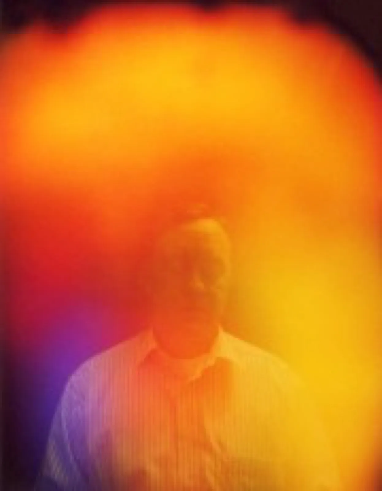 Aurafoto eines Mannes in hellem, gestreiftem Hemd vor dunklem Hintergrund. Ein kräftiger orange-gelber Farbschleier umgibt Kopf und Oberkörper, links unten mit einem violett-blauen Anteil.