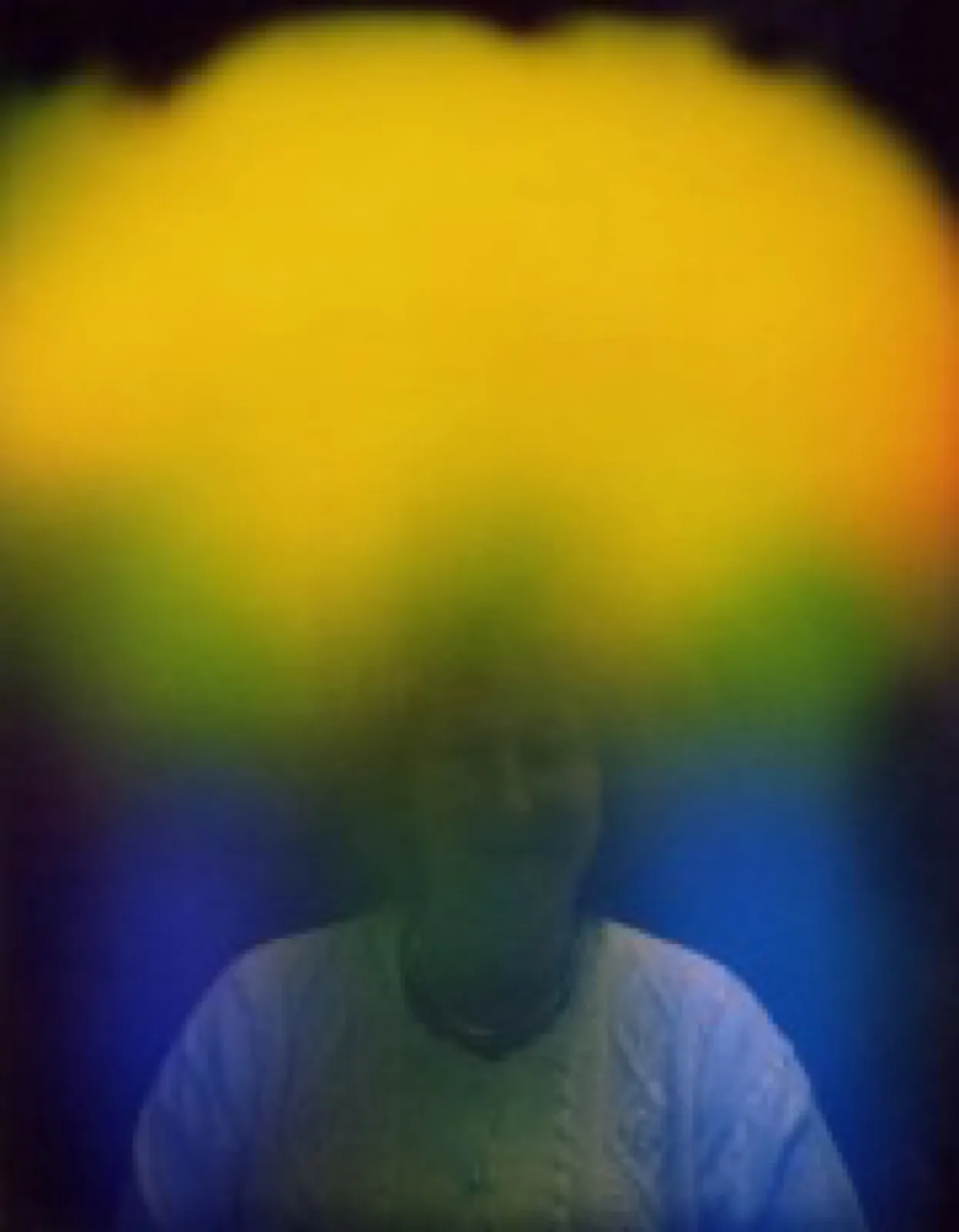 Aurafoto von 1997: Porträt einer Person in hellem Pullover, über dem Kopf ein breiter gelber Farbschleier, der seitlich in Grün und Blau übergeht.