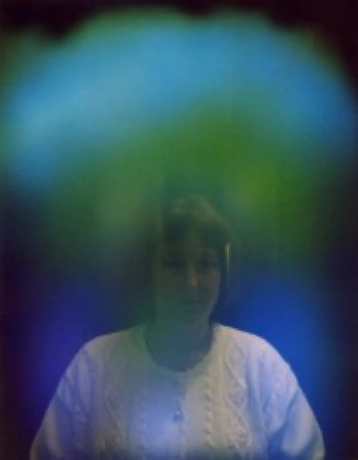 Aurafoto von 1997: Porträt einer Frau mit dunklem Haar in weißem Strickpullover, umgeben von einem türkis- und grünlichen Lichtschleier über dem Kopf und Blau zu beiden Seiten.