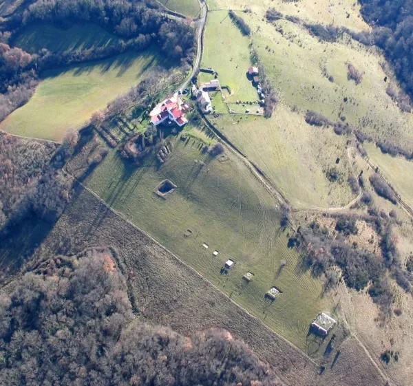 Luftaufnahme einer grünen Hügellandschaft in Südfrankreich mit einem Bauernhaus mit rotem Dach und einer Reihe von Horus-Energiepyramiden, die lange Schatten über den Hang werfen