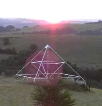 Die 9-Meter-Energiepyramide bei Sonnenuntergang mit einem großen rosa-roten runden Lichtreflex (Blendenfleck)