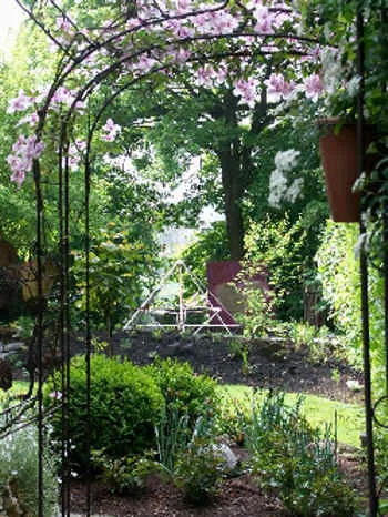 Blick durch einen rosenberankten Torbogen auf eine Energiepyramide Modell C im Garten (Ehekirchen bei Augsburg)