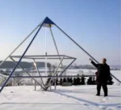 Dr. Mansmann steht neben seiner Energiepyramide Modell F in einer Schneelandschaft