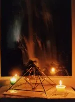 Energiepyramide Modell A zwischen zwei brennenden Kerzen vor einem dunklen, dramatischen Hintergrund
