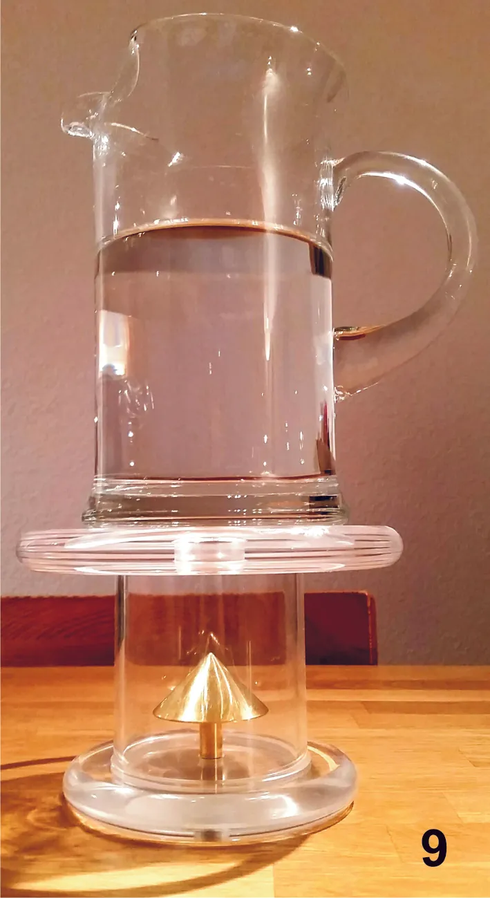 Glaskrug mit Wasser auf einer Acrylsäule, in der ein goldener Energiekegel steht