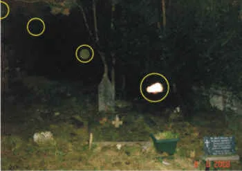 Nächtliches Friedhofsfoto mit Grabsteinen; mehrere gelb markierte Lichtflecke (Orbs)