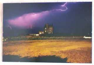 Foto „Blitz & Donner Quiberon": ein Herrenhaus bei Nacht unter violettem Himmel mit Blitzen über einem Feld