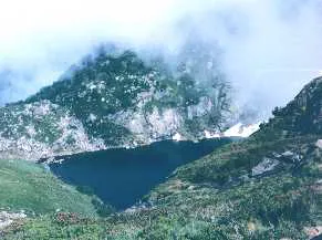 Ein dunkler Bergsee in einem nebelverhangenen Felskessel der Pyrenäen.