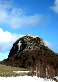 Der Montségur-Felskegel („Pog") mit der Burgruine auf dem Gipfel, von unten gesehen; am Himmel ein Gleitschirm, im Vordergrund Schnee.