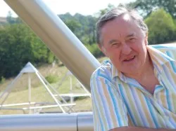 D. Harald Alke, grauhaariger Gründer des Kyborg Instituts im gestreiften Hemd, lächelnd an einem hellen Gerüst einer Horus Energiepyramide im Freien