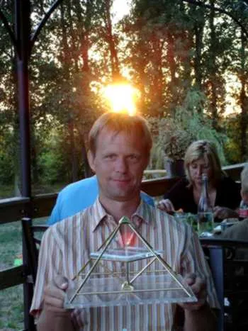 Ein Mann hält eine kleine Horus-Energiepyramide; die untergehende Sonne steht genau hinter seinem Kopf wie ein Heiligenschein, an einem Gartentisch