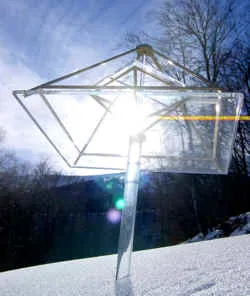 Foto von Modell A auf einer Acrylsäule im Schnee mit Sonnenreflex und einem waagerechten gelben Lichtstreifen