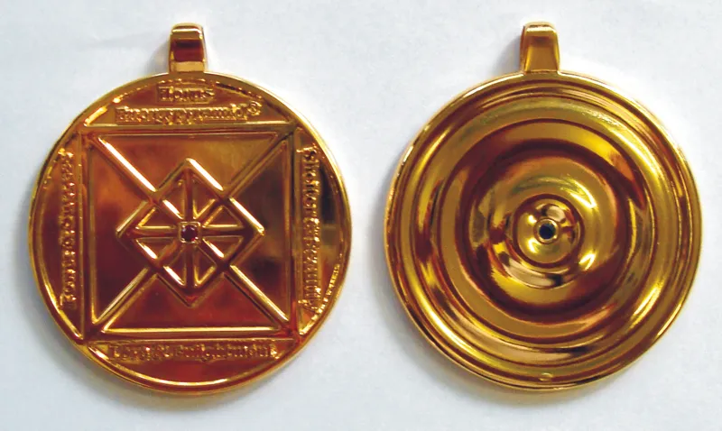 Das goldene Horus-Schutzamulett von beiden Seiten: vorne das achteckige Bagua-Mandala mit Strahlenstern und rotem Rubin in der Mitte, hinten konzentrische Wellenringe mit einem blauen Saphir.