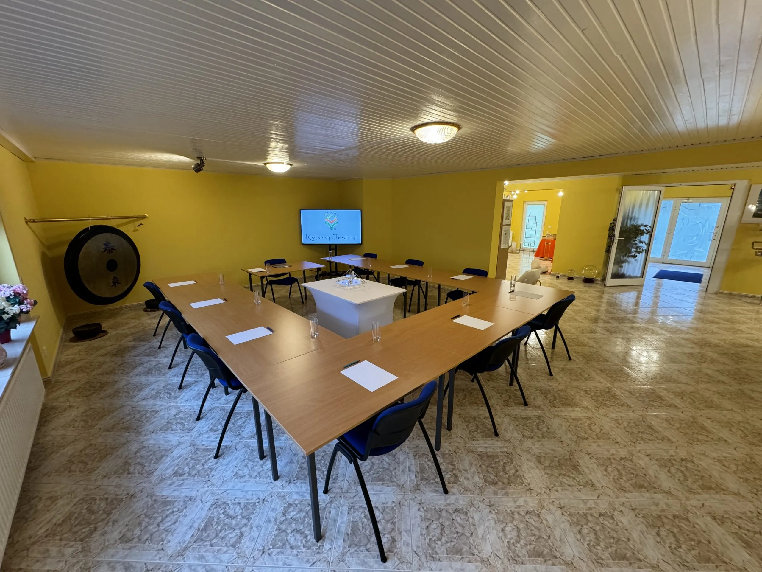 Weitwinkelblick in den Trainings- und Seminarraum des Kyborg Instituts mit U-förmiger Tischanordnung, Gong an der Wand und Bildschirm mit Kyborg-Logo; im Hintergrund ein hellerer Nebenraum