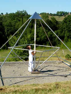Eine Frau in weißer Kleidung steht im Metallrahmen der Modell-E-Energiepyramide auf dem Feld von Le Braquet